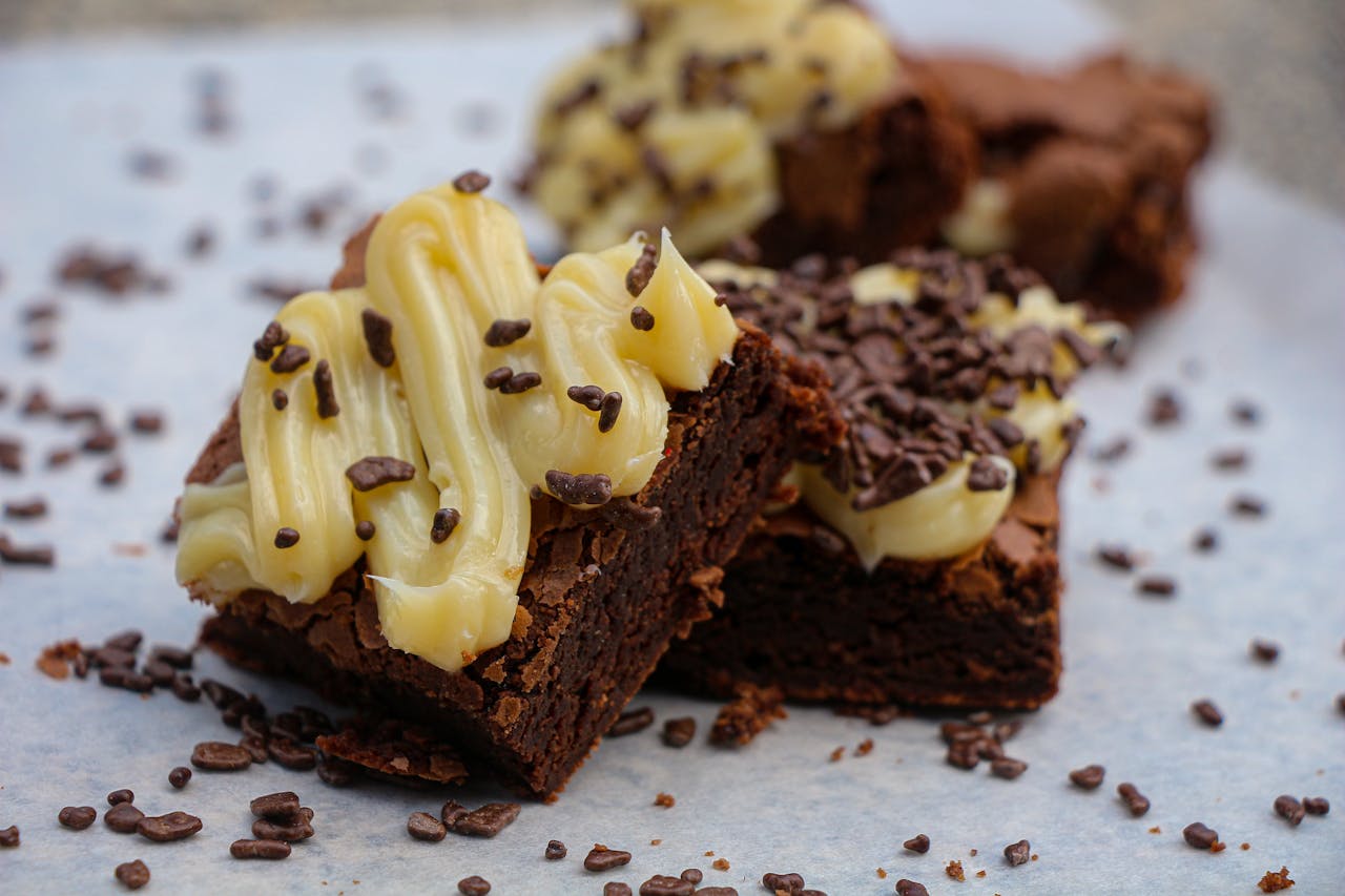 Close-up of rich chocolate brownies topped with creamy frosting and sprinkles.